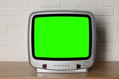 Image of Retro Tv set with green screen on wooden table near white brick wall. Chroma key