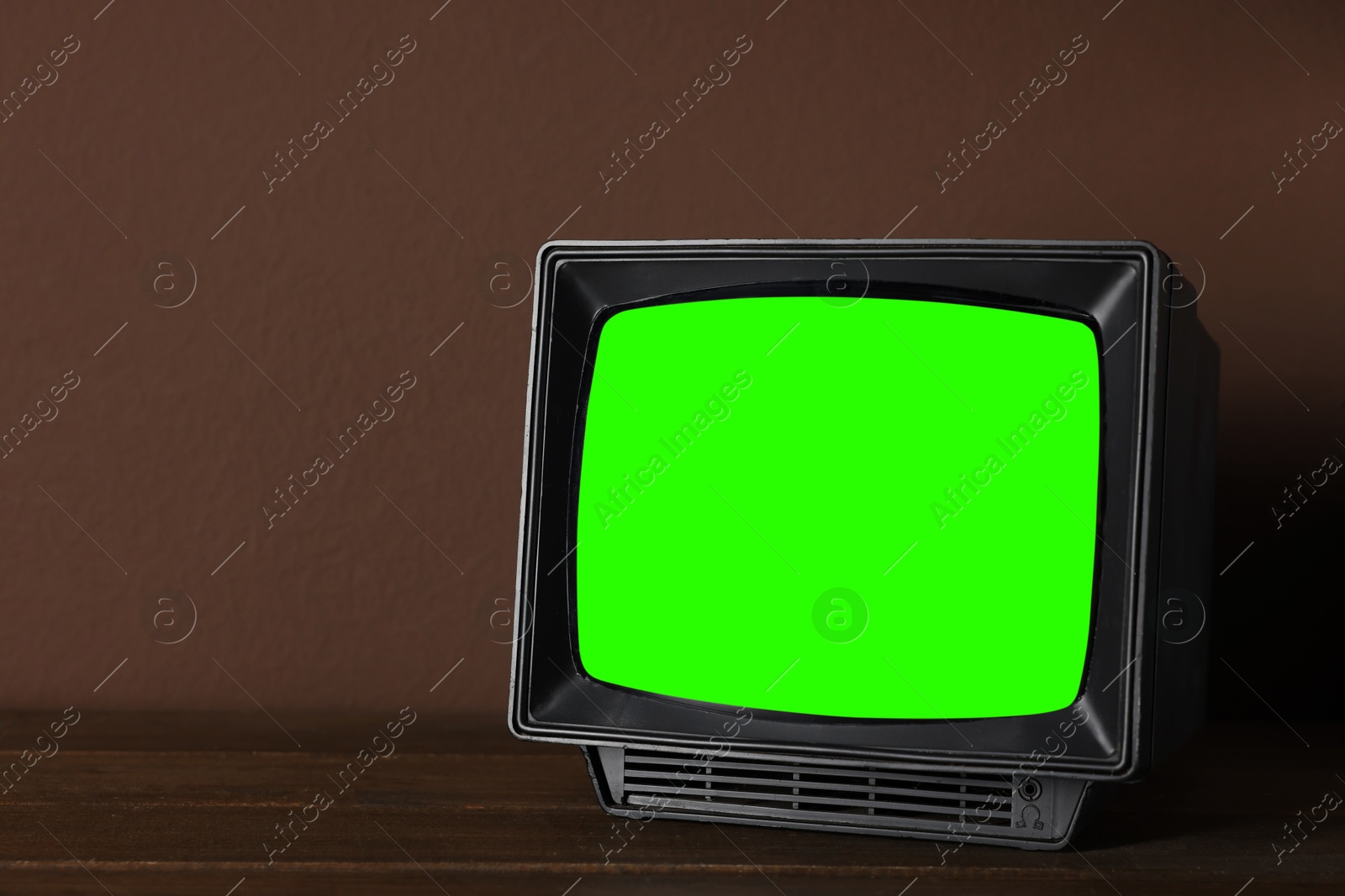 Image of Retro Tv set with green screen on wooden table near brown wall, space for design. Chroma key