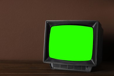 Image of Retro Tv set with green screen on wooden table near brown wall, space for design. Chroma key