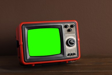 Image of Retro Tv set with green screen on wooden table near brown wall, space for design. Chroma key