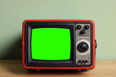 Image of Retro Tv set with green screen on wooden table near pale color wall. Chroma key