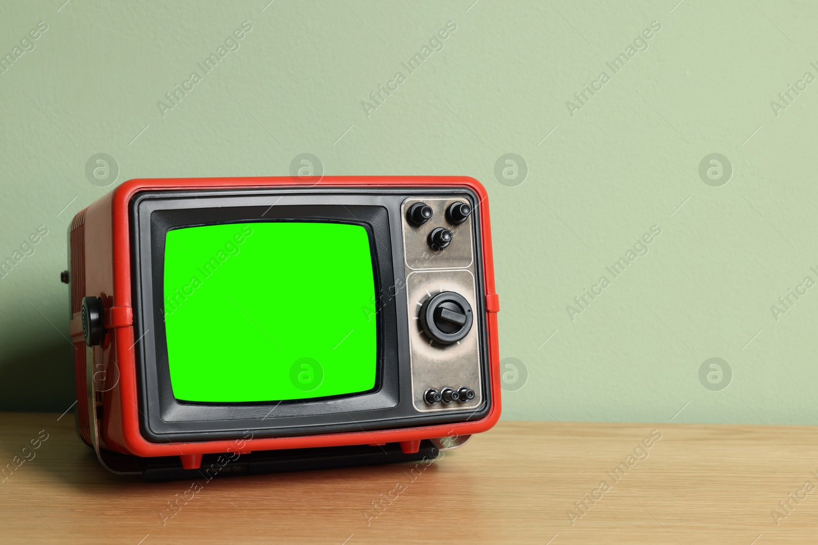 Image of Retro Tv set with green screen on wooden table near color wall, space for design. Chroma key