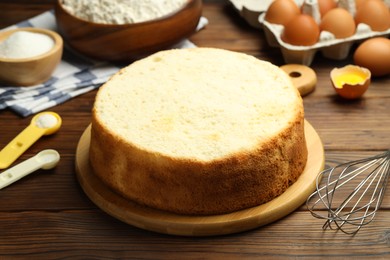 Photo of Tasty cut sponge cake, whisk and ingredients on wooden table