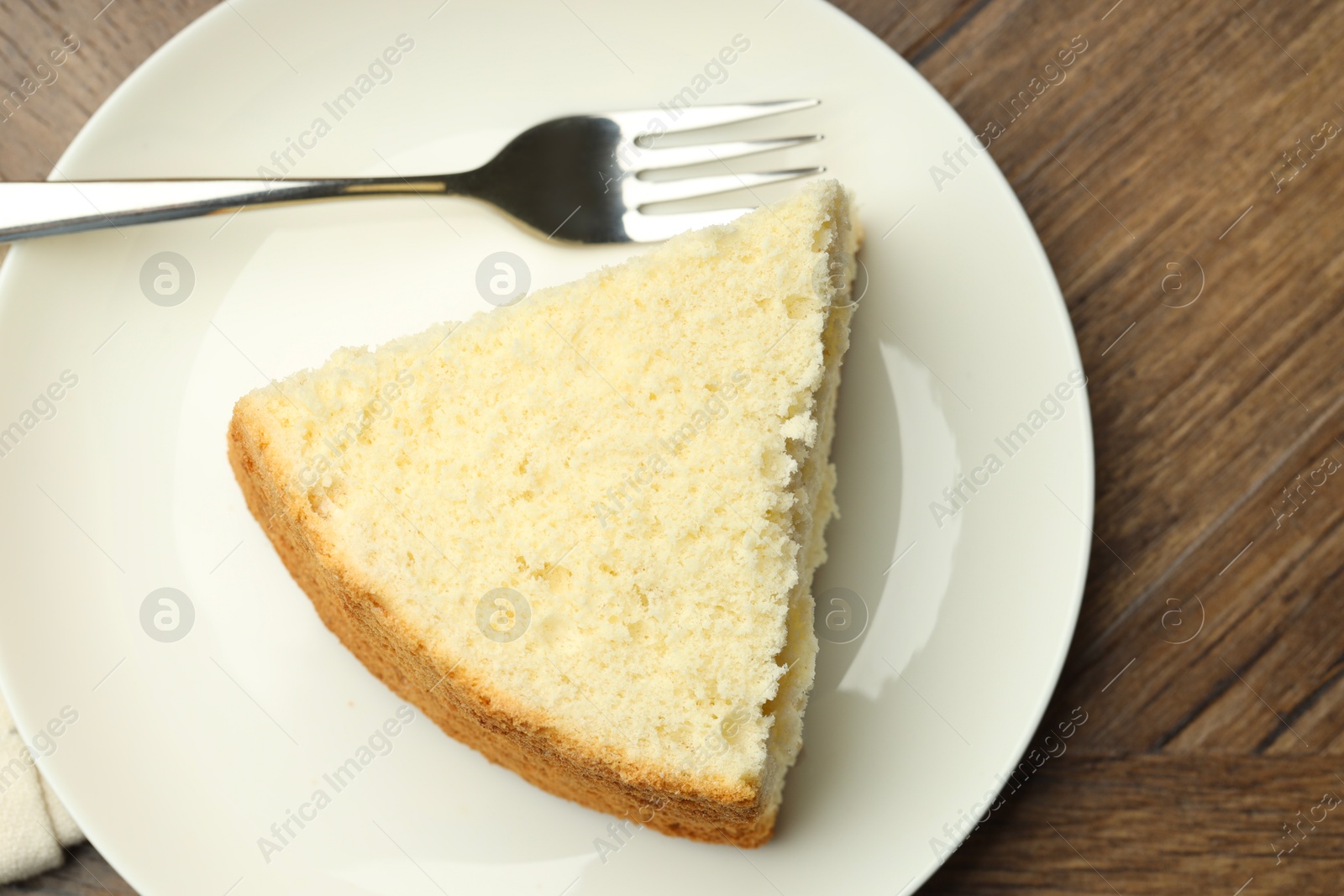 Photo of Piece of delicious sponge cake and fork on wooden table, top view