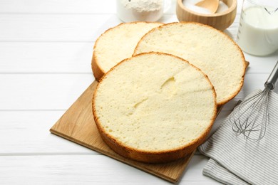 Photo of Delicious cut sponge cake, whisk and ingredients on white wooden table