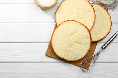 Photo of Delicious cut sponge cake and whisk on white wooden table, flat lay. Space for text