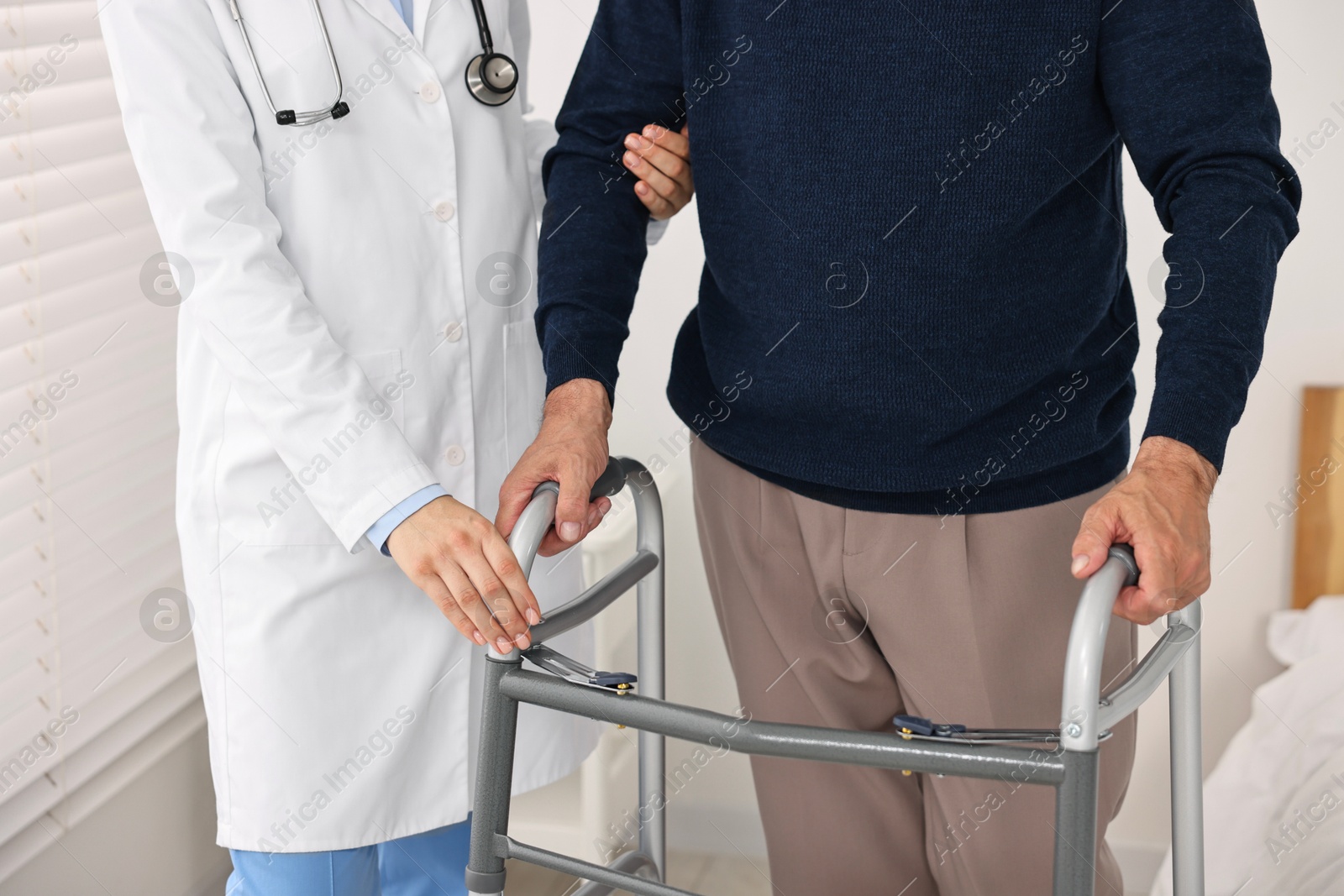 Photo of Doctor helping senior man with walking frame in clinic, closeup