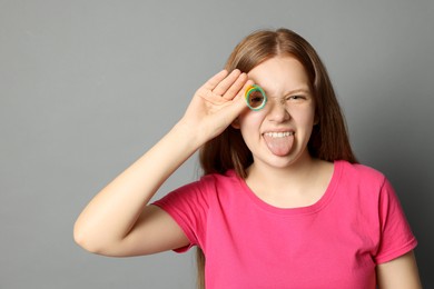 Photo of Happy teenage girl with tasty rainbow sour belt showing her tongue on grey background