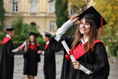 Photo of Happy students with diplomas after graduation ceremony outdoors, selective focus