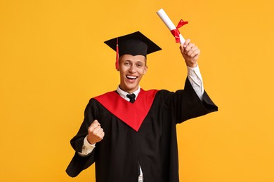 Happy student with diploma after graduation on orange background