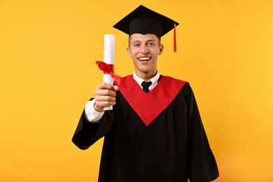 Photo of Happy student with diploma after graduation on orange background