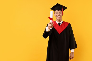 Photo of Happy student with diploma after graduation on orange background. Space for text