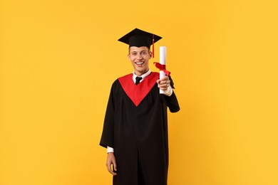 Photo of Happy student with diploma after graduation on orange background