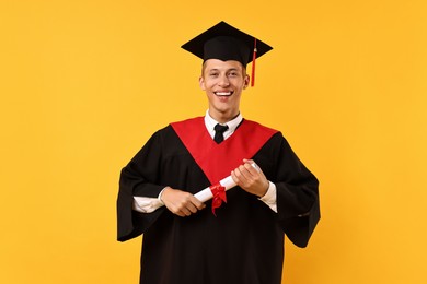 Photo of Happy student with diploma after graduation on orange background