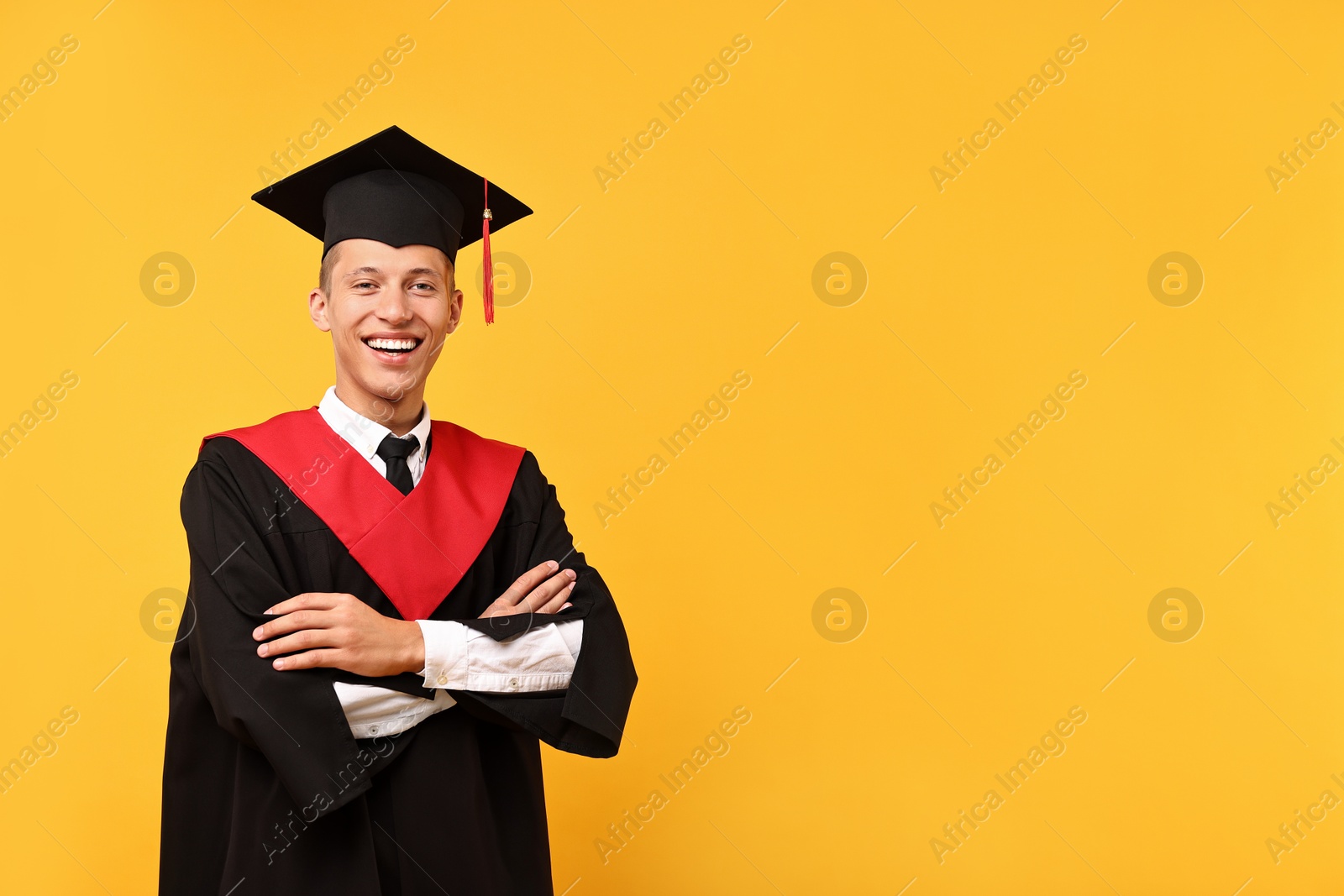 Photo of Happy student with crossed arms after graduation on orange background. Space for text