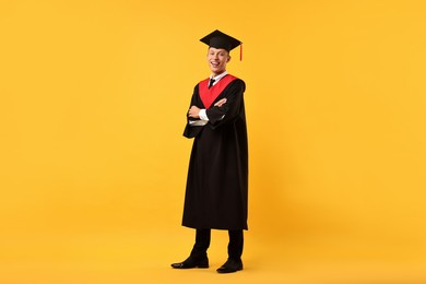 Photo of Happy student with crossed arms after graduation on orange background