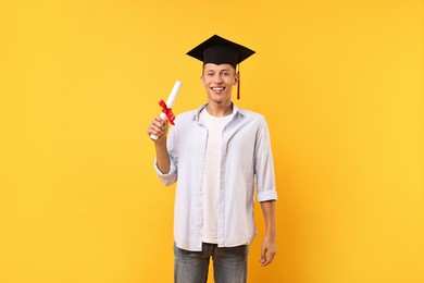 Happy student with diploma after graduation on orange background