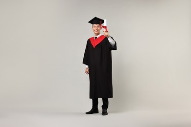 Photo of Happy student with diploma after graduation on grey background