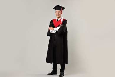 Happy student with diploma after graduation on grey background