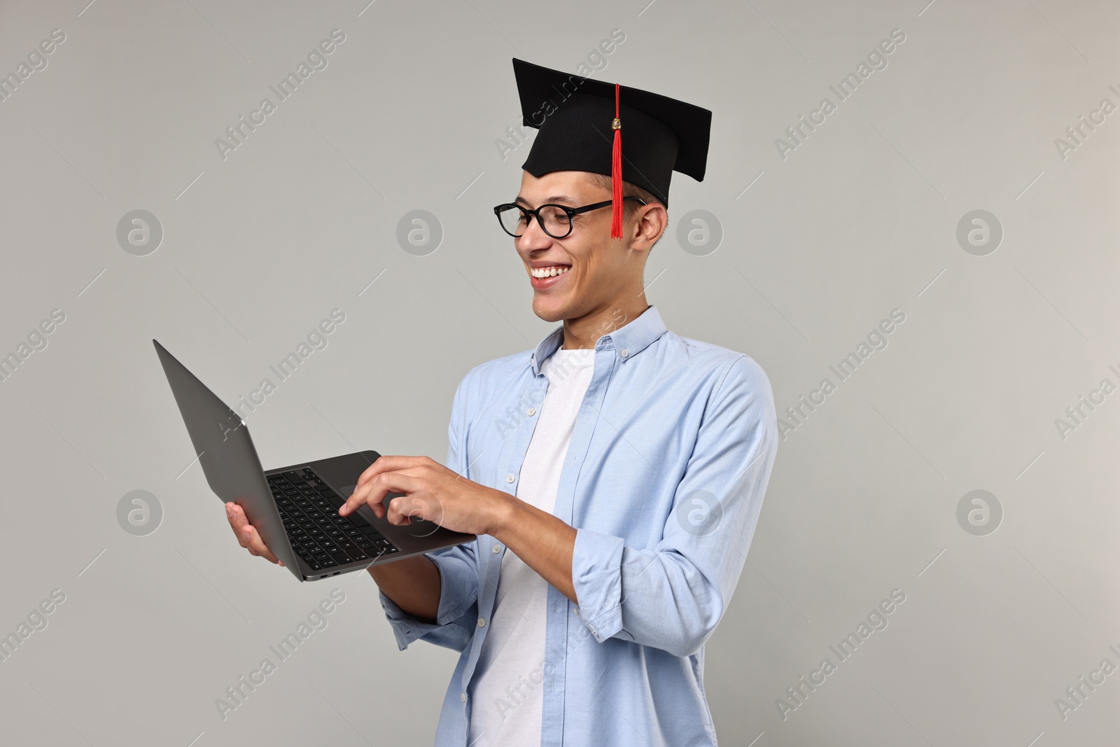 Photo of Happy student with laptop after graduation on grey background