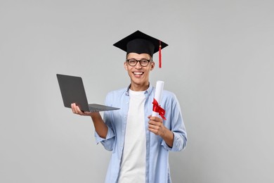 Photo of Happy student with diploma and laptop after graduation on grey background