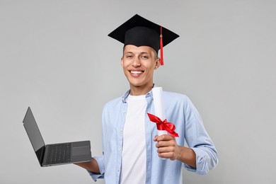 Photo of Happy student with diploma and laptop after graduation on grey background