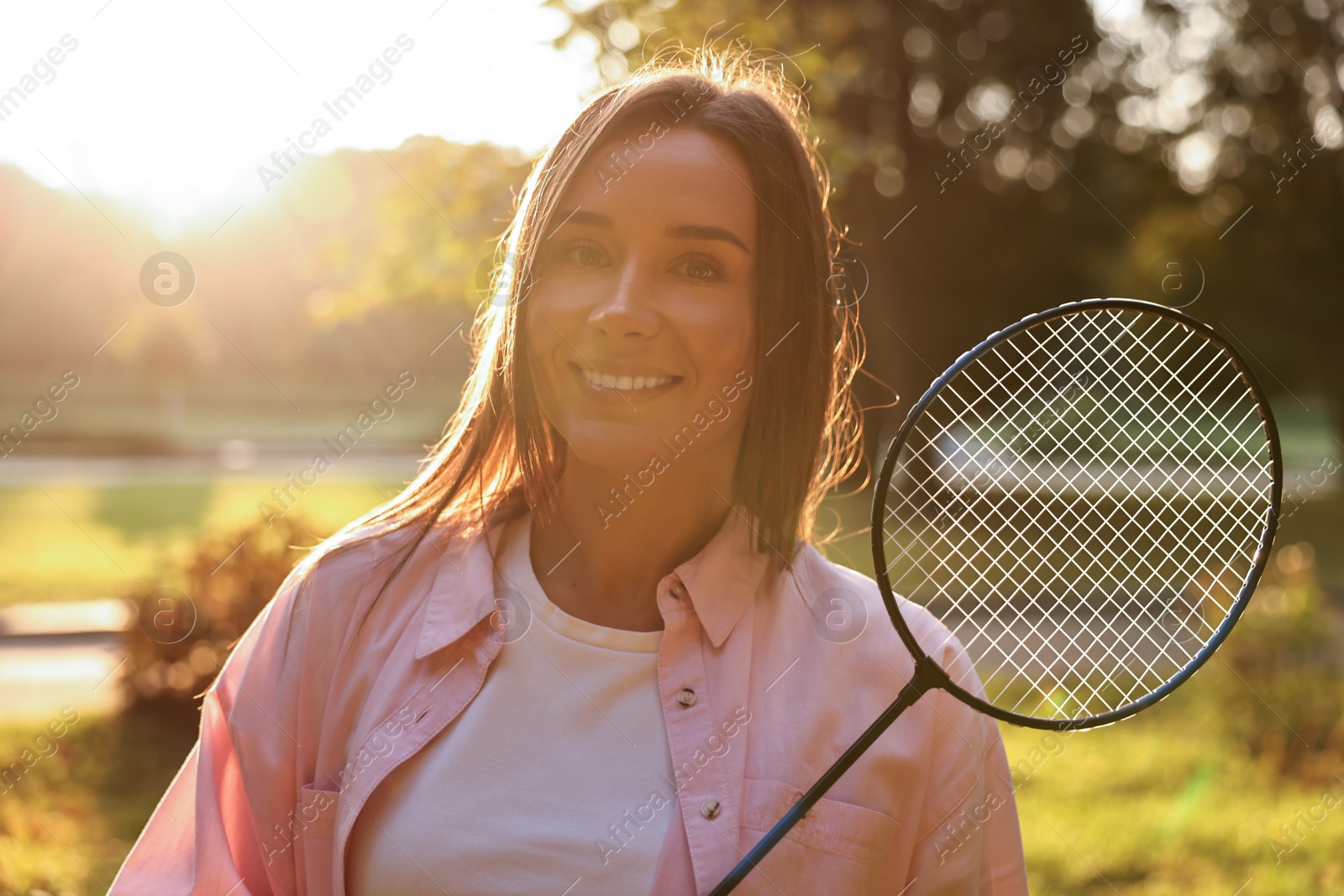 Photo of Happy young woman with badminton racket in park on sunny day