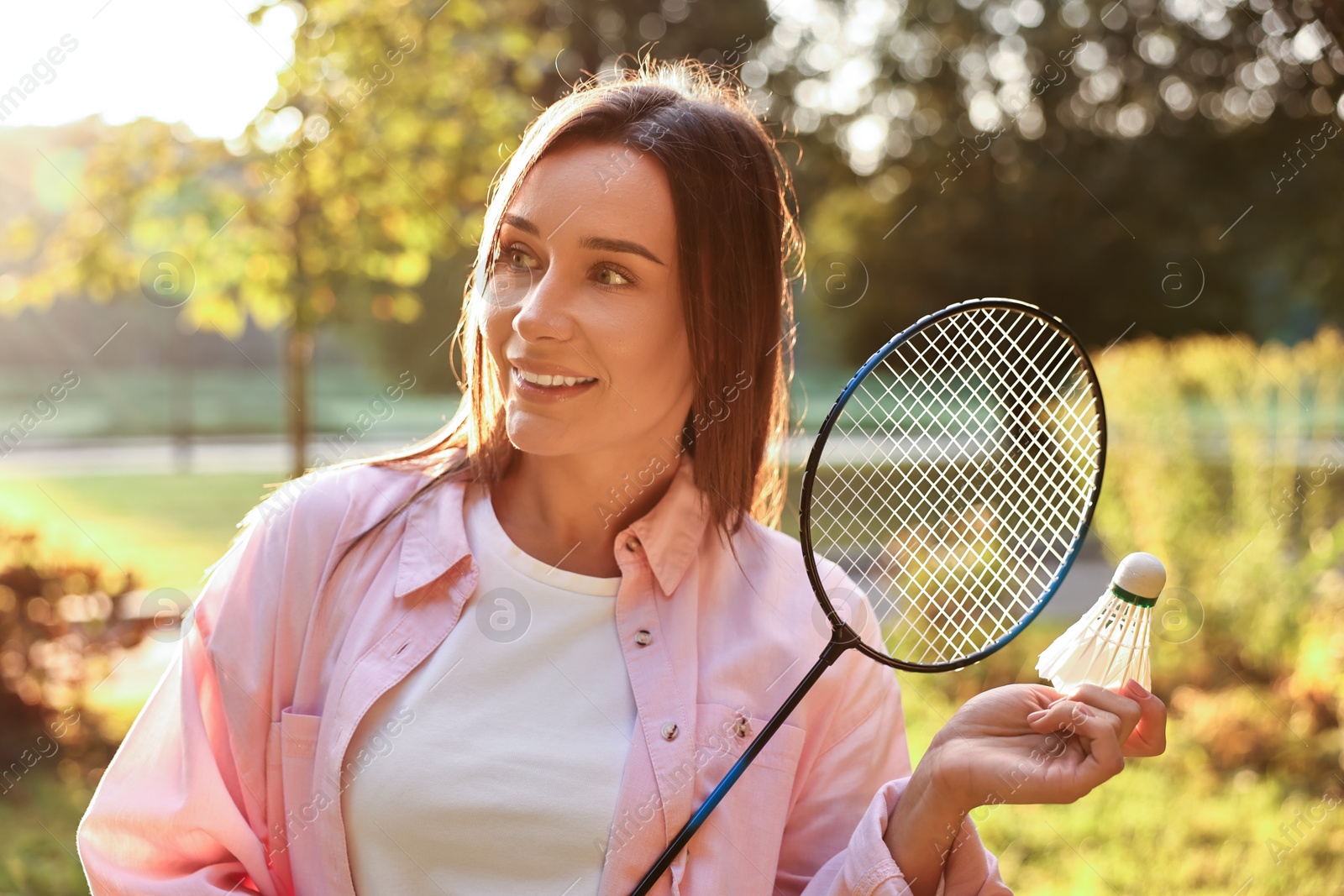 Photo of Happy young woman with badminton racket and shuttlecock in park on sunny day