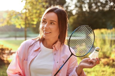 Happy young woman with badminton racket and shuttlecock in park on sunny day