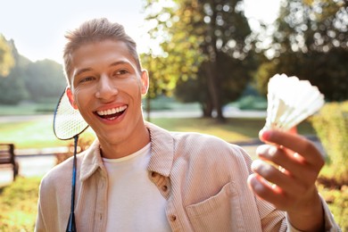 Photo of Happy young man with badminton racket and shuttlecock in park on sunny day