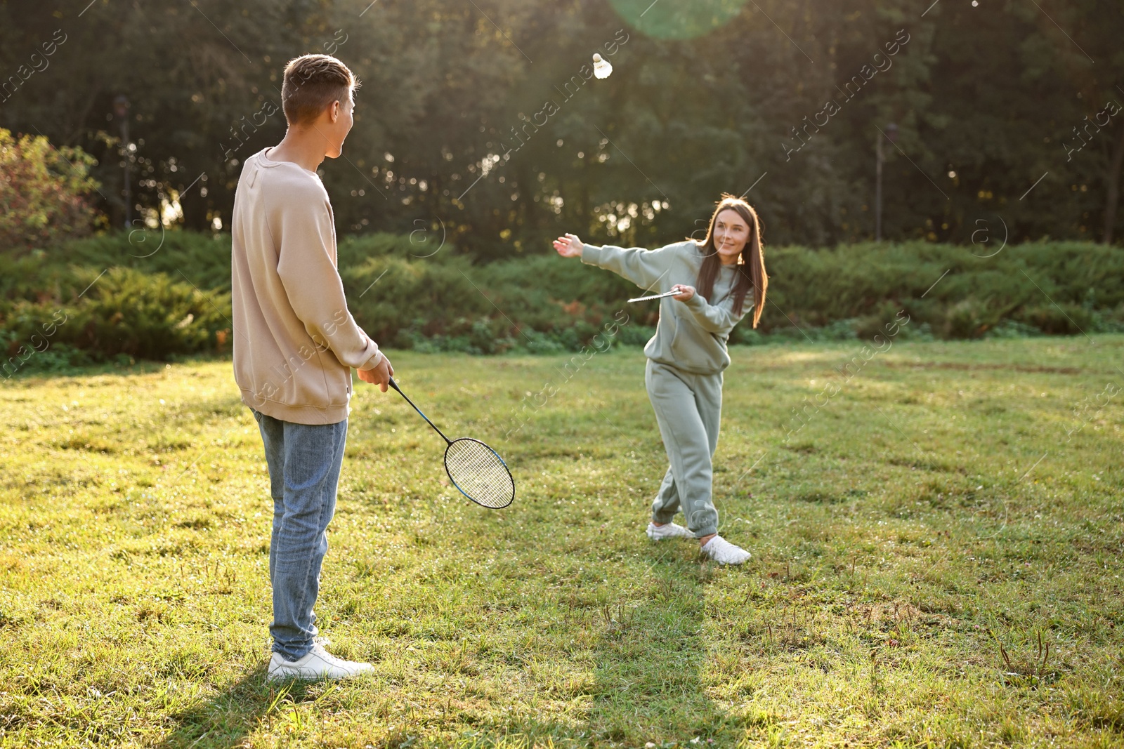 Photo of Young woman and man playing badminton in park on sunny day, selective focus