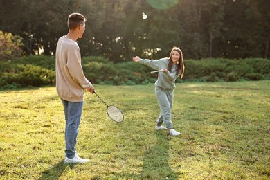 Photo of Young woman and man playing badminton in park on sunny day, selective focus