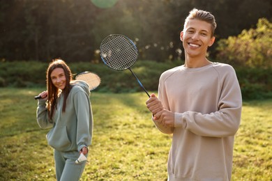 Photo of Young man and woman with badminton rackets and shuttlecock in park on sunny day, selective focus