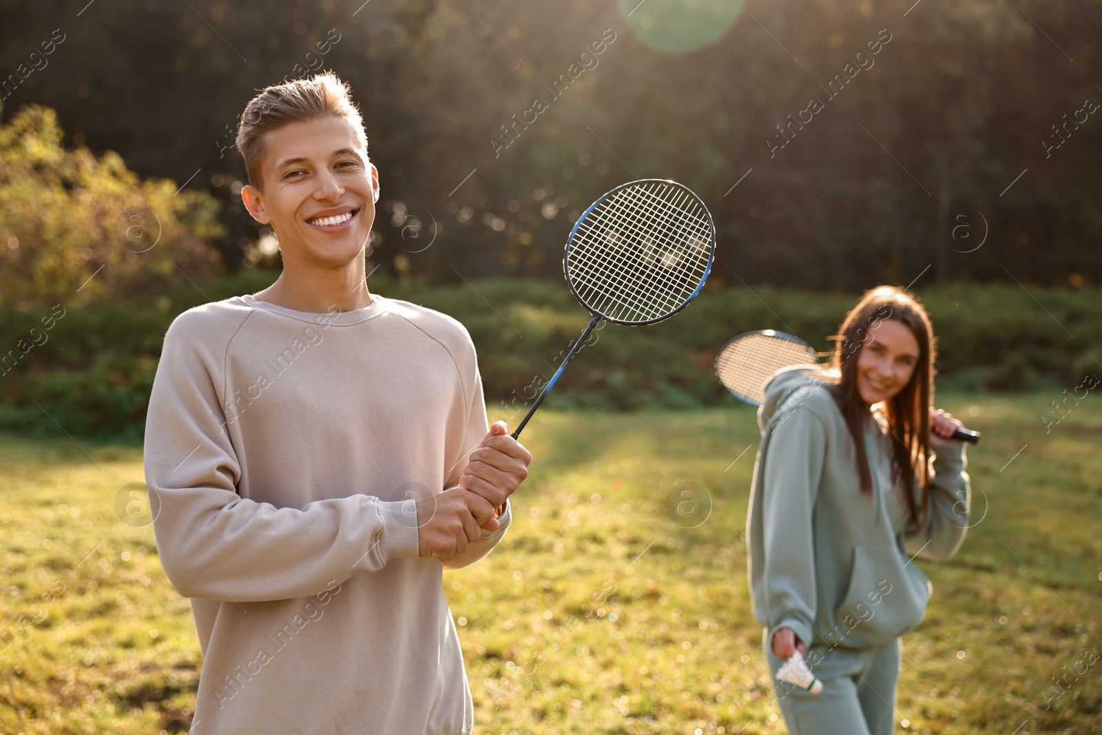 Photo of Young man and woman with badminton rackets and shuttlecock in park on sunny day, selective focus