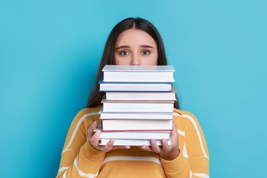 Photo of Young student with stack of books having stress before exam on light blue background