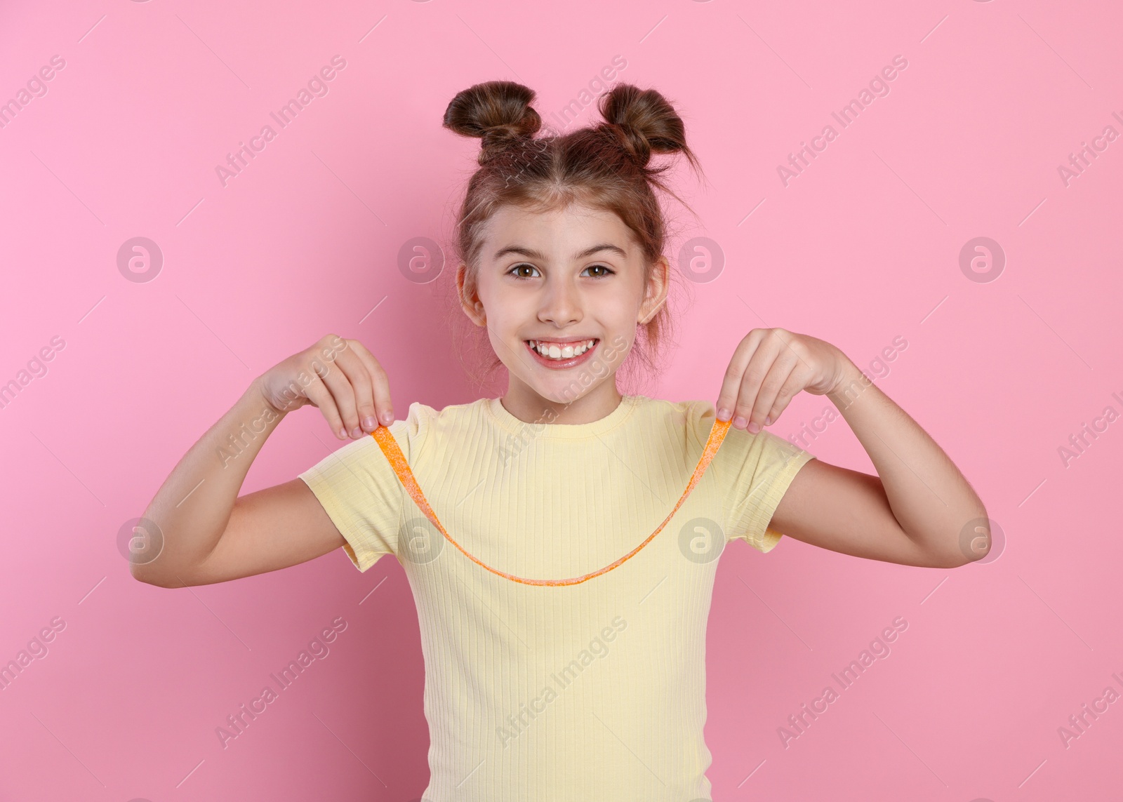 Photo of Happy girl showing tasty gummy candy on pink background