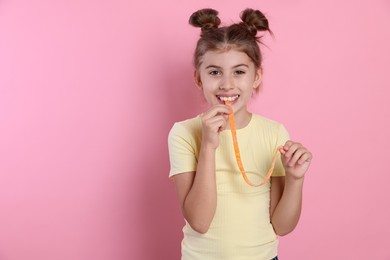 Happy girl eating tasty gummy candy on pink background. Space for text