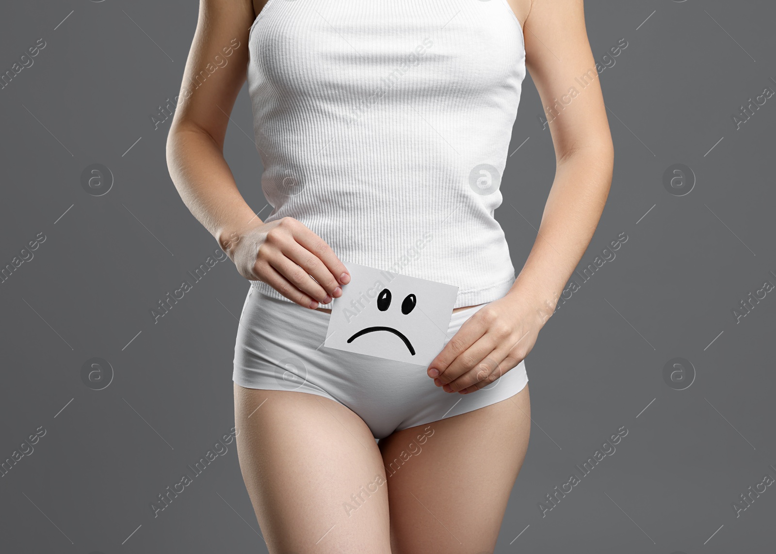 Photo of STD (sexually transmitted disease). Woman holding sticky note with drawn sad face on grey background, closeup