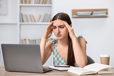 Photo of Tired student preparing for exam with laptop at table indoors