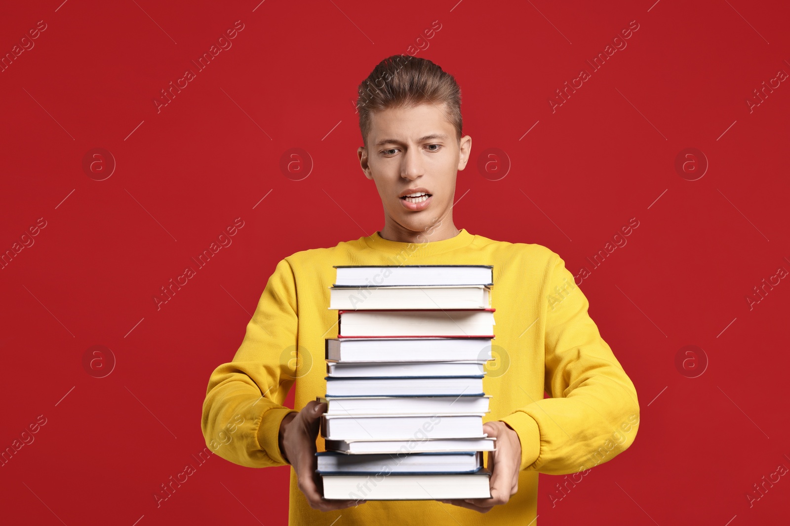 Photo of Emotional student with stack of books having stress before exam on red background