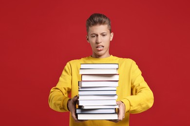 Photo of Emotional student with stack of books having stress before exam on red background