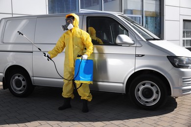 Photo of Pest control worker with spray tank near gray minibus outdoors