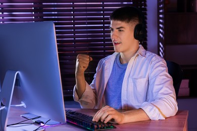 Photo of Young man playing video game with keyboard at wooden table indoors