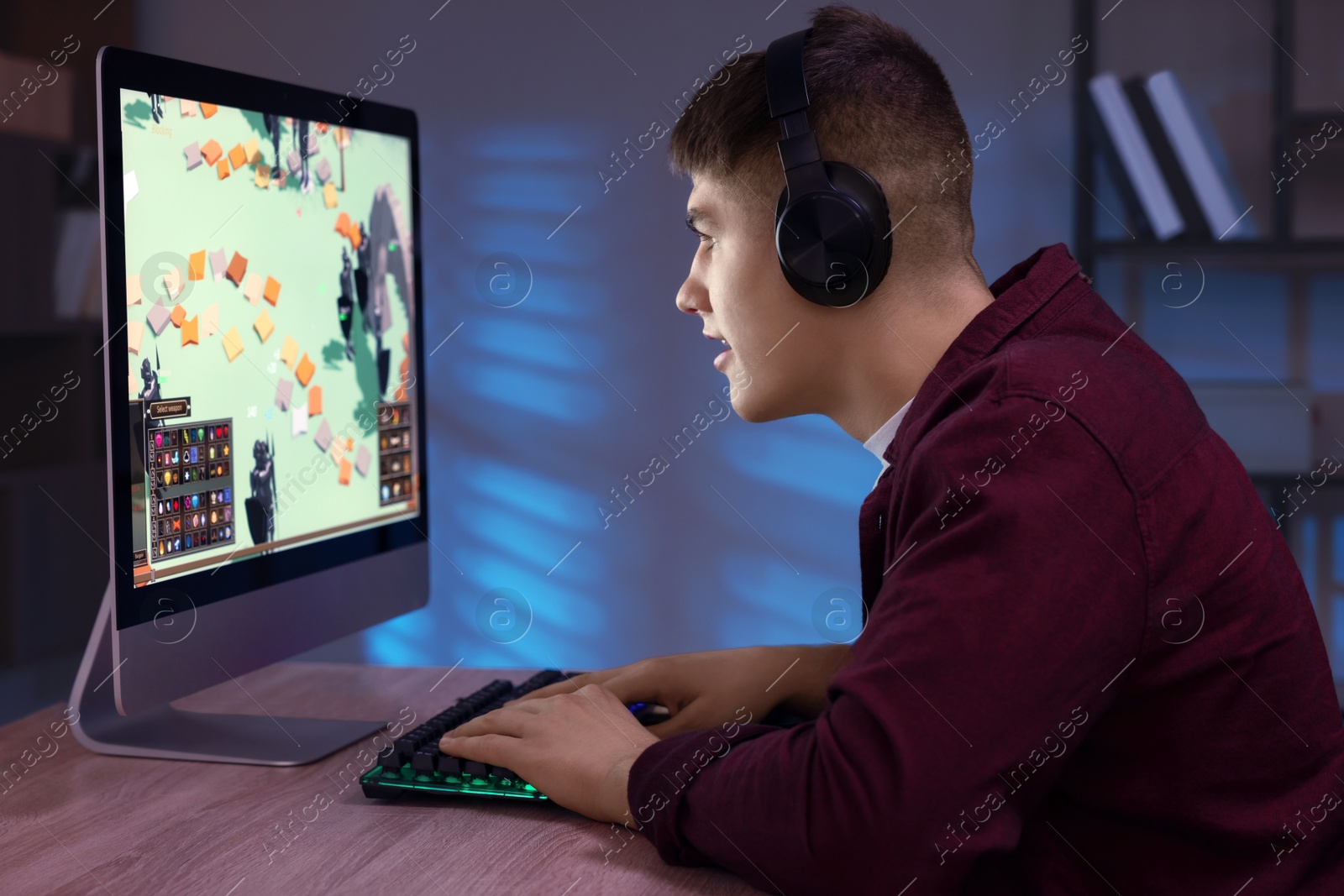 Photo of Young man playing video game with keyboard at wooden table indoors