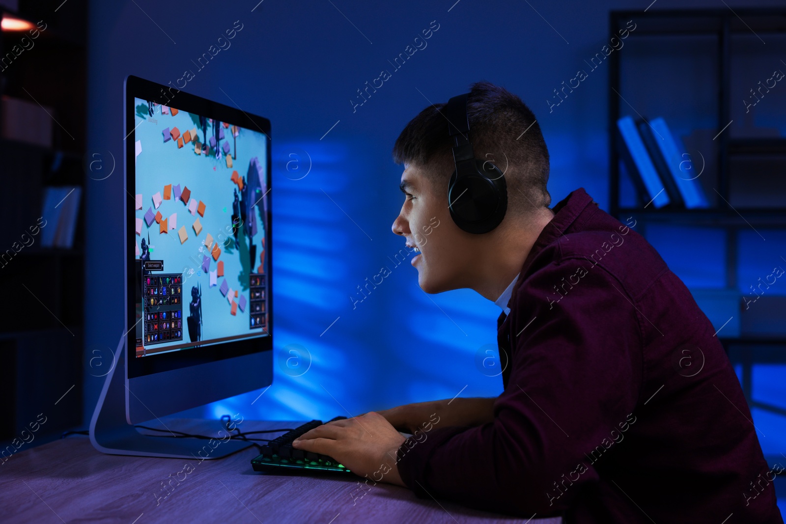 Photo of Young man playing video game with keyboard at wooden table indoors