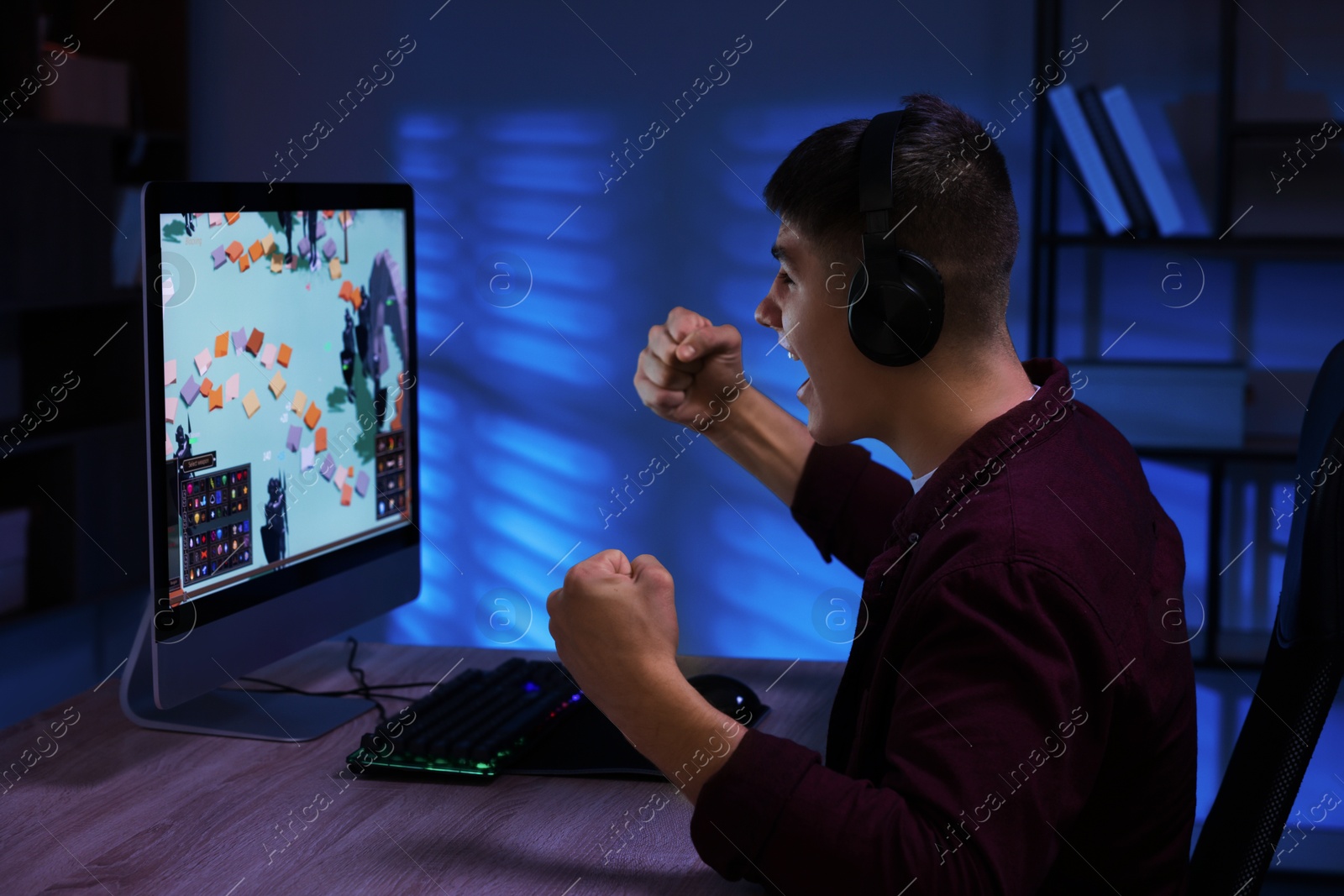 Photo of Emotional young man playing video game with keyboard at wooden table indoors