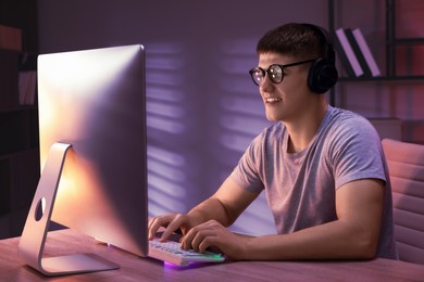 Photo of Young man playing video game with keyboard at wooden table indoors