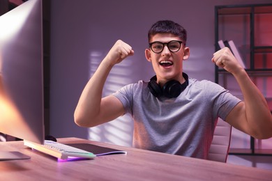 Photo of Emotional young man playing video game with keyboard at wooden table indoors