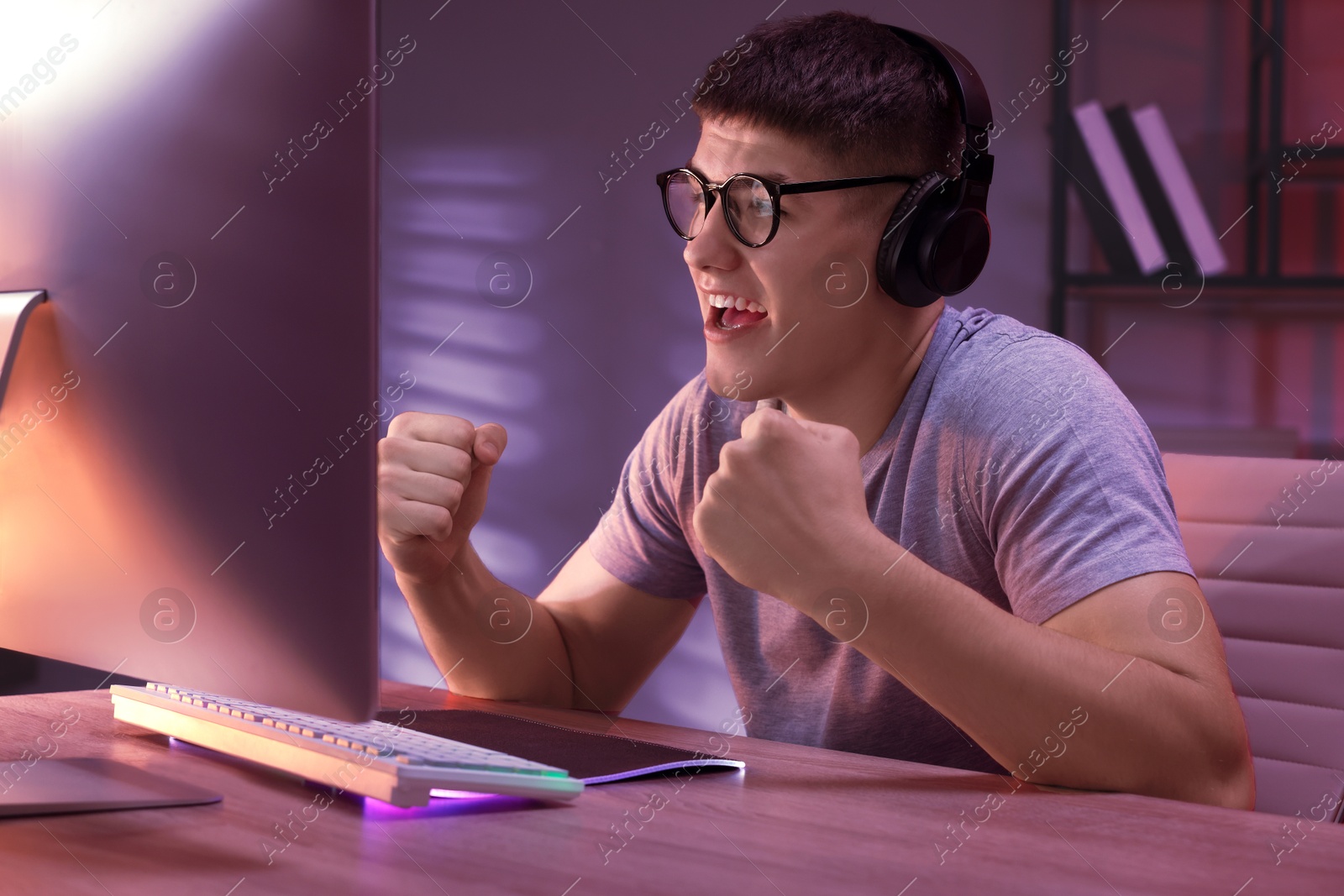 Photo of Young man playing video game with keyboard at wooden table indoors