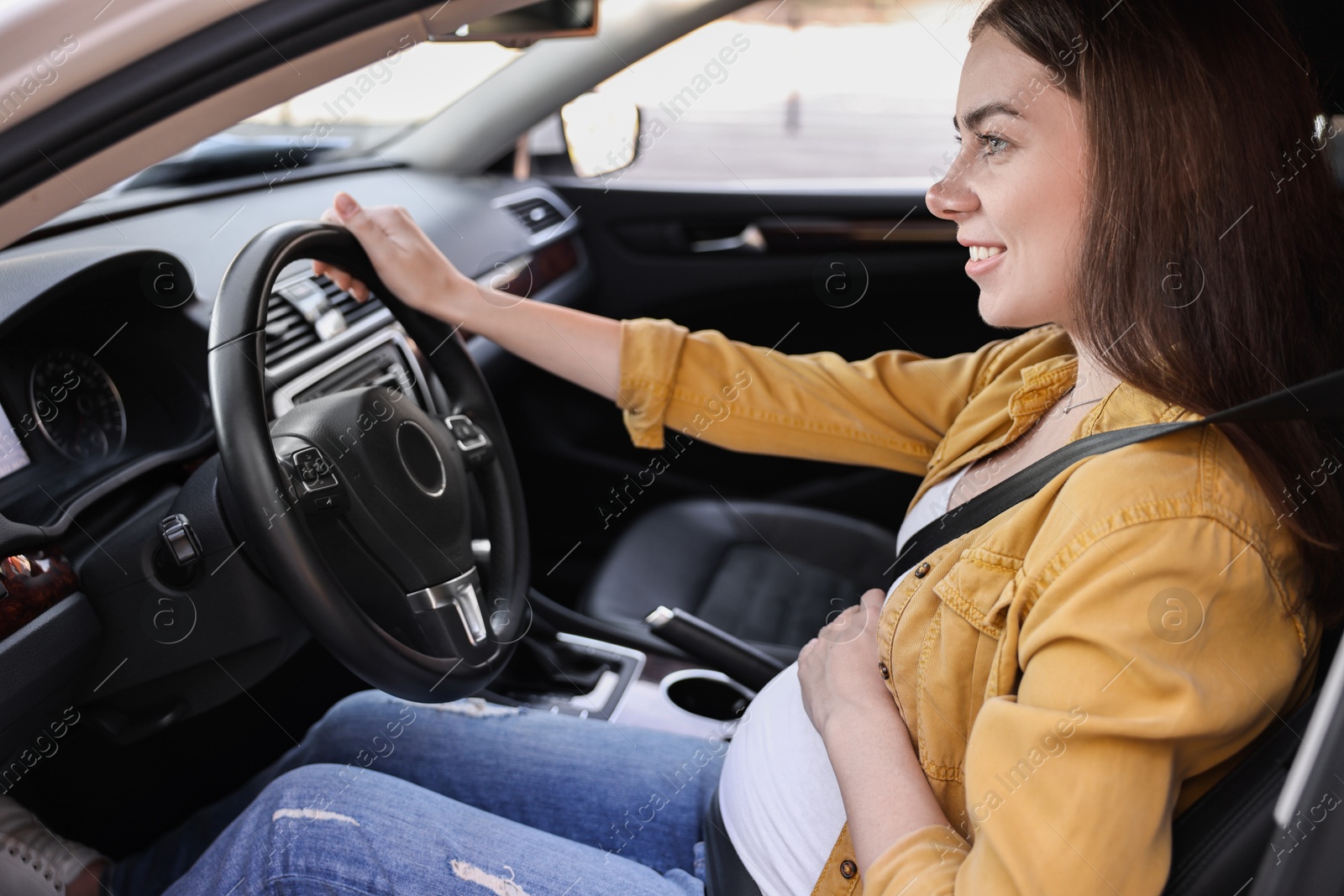 Photo of Smiling pregnant woman with safety belt driving car